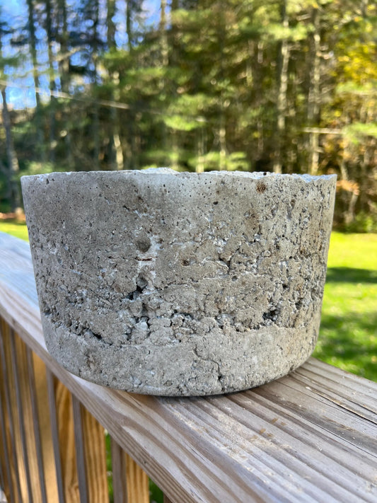 Concrete pot on a wooden surface with a natural background of trees and grass.
