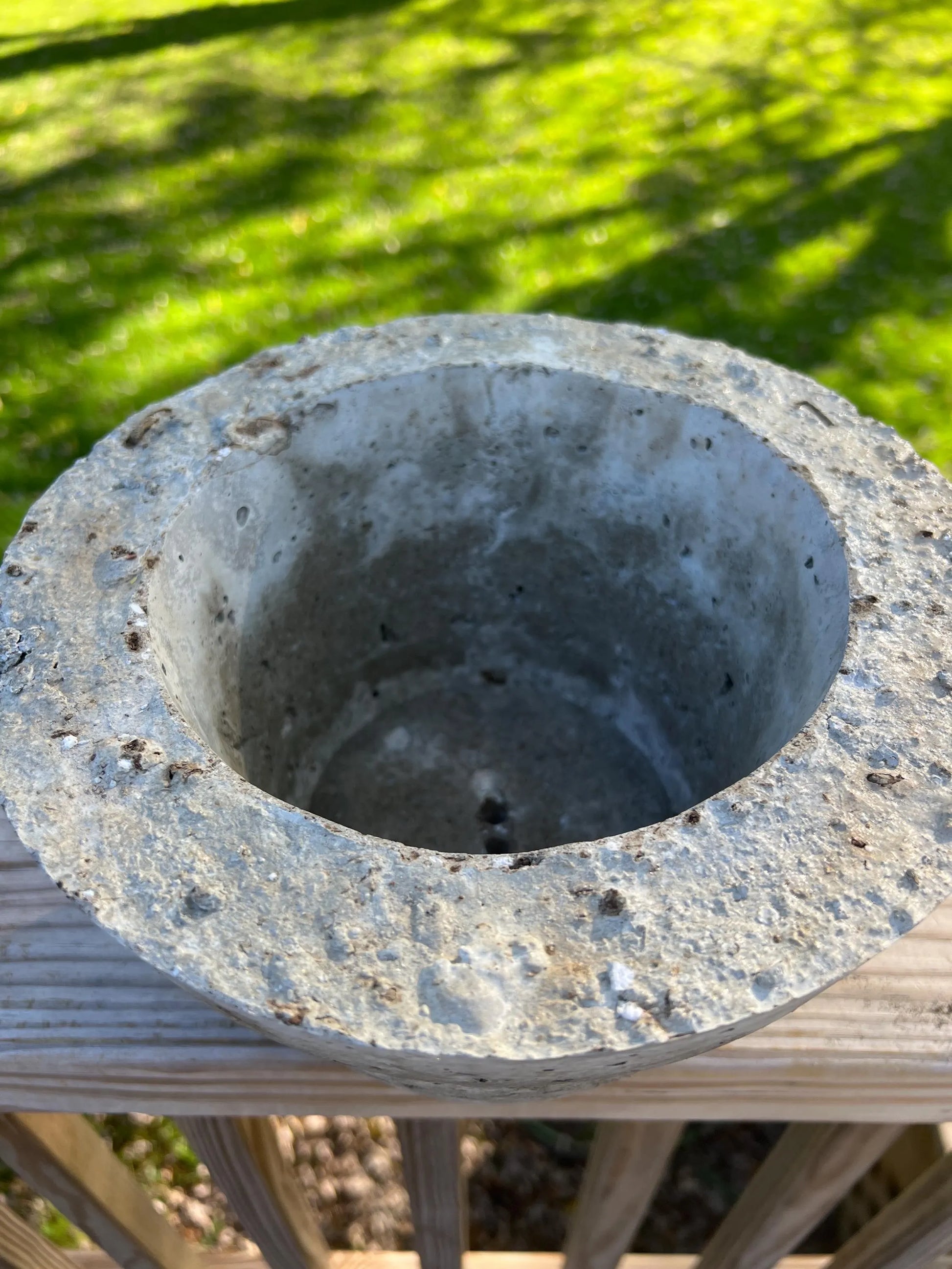 Concrete flower pot on a wooden surface with grass in the background