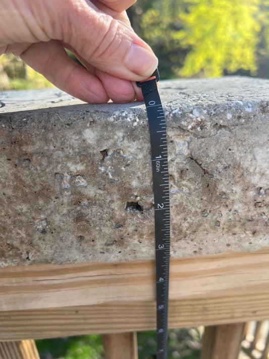 Hand holding a measuring tape against a concrete surface with blurred greenery in the background