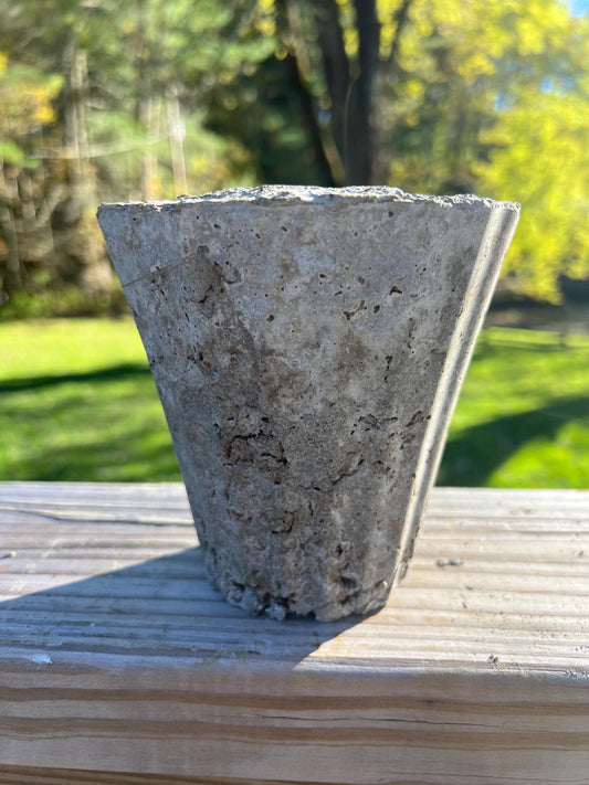 Concrete flower pot on a wooden surface with a blurred green outdoor background