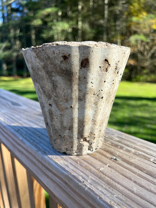 Concrete flower pot on a wooden deck with a blurred green outdoor background