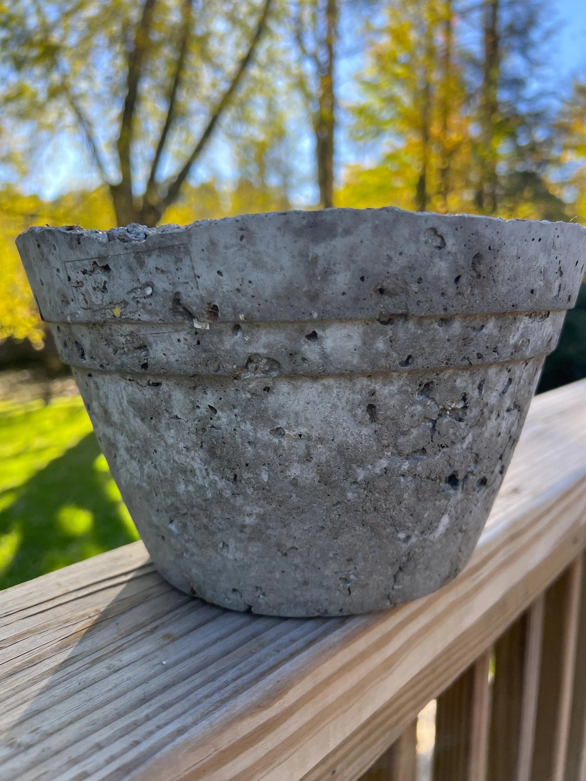 Concrete pot on a wooden railing with a blurred natural background